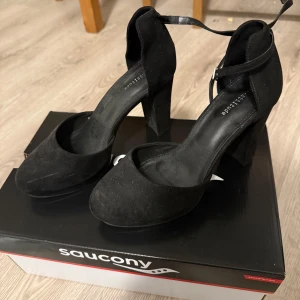 Svarta klackskor med ankelrem - Snygga svarta klackskor  med ankelrem och hög klack. Perfekta för en elegant look. Skorna har en rund tå. Behöver en avdammning innan använd ning.