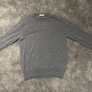 Grå merinoull tröja - Säljer en stilren grå merinoull tröja. Tröjan har en klassisk rund hals och långa ärmar. Perfekt för en minimalistisk look. Det står att tröjan är storlek L men passar som XS/S, 9/10 skick, hör av er vid minsta lilla