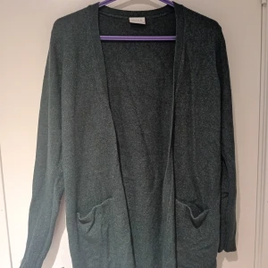 Mörkgrå kofta från Zara - Säljer en stilren mörkgrön kofta från Zara. Den har en öppen design med långa ärmar och två praktiska fickor framtill. Perfekt för lager-på-lager under kyligare dagar.