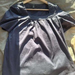 Mörkblå blus från Esprit - Säljer en stilren mörkblå blus från Esprit. Blusen har korta ärmar och en fyrkantig halsringning med veckade detaljer. Perfekt för en avslappnad men ändå elegant look.