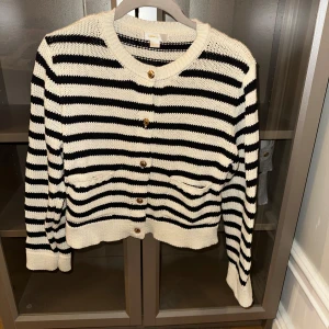 Randig kofta med knappar - Säljer en snygg randig kofta i svart och vit med knappar framtill. Koftan har långa ärmar och en rund halsringning. Perfekt för en stilren look.