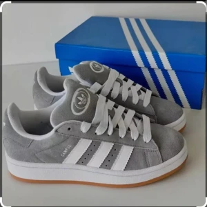 Grå Adidas campus 00 - Snygga grå Adidas campus sneakers i mocka med vita detaljer och klassiska tre ränder på sidan. Skorna har en gummisula och snörning framtill. Perfekta för en stilren look.