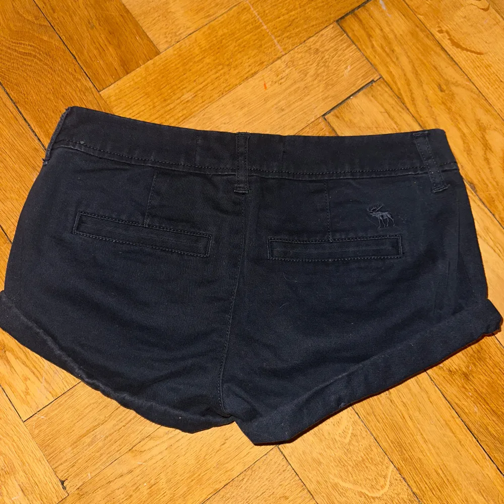 Snygga svarta shorts från Abercrombie & Fitch med knapp och dragkedja framtill. De har två framfickor och två bakfickor, samt en liten broderad logga på baksidan. Perfekta för en avslappnad stil. Low waist . Shortsit.