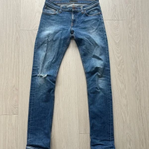 Blå jeans från Nudie Jeans - Snygga blå jeans från Nudie Jeans (grim Tim) med en klassisk femficksdesign. De har en lätt slitning på knäet som är från fabrik och en bekväm passform. Perfekta för en avslappnad stil.