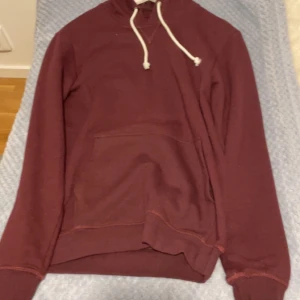 Vinröd hoodie från Pier One - Säljer en snygg vinröd hoodie från Pier One. Den har en klassisk design med en känguruficka och justerbar huva med vita snören. Perfekt för en avslappnad stil.