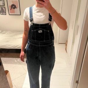 Mörkblå denim hängselbyxor från Monki - Snygga mörkblå hängselbyxor i denim från Monki. Byxorna har justerbara axelband och flera praktiska fickor både fram och bak. Säljer pga för korta för mig, (är 173)