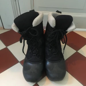 Svarta vinterstövlar från Sorel stl 40 - Säljer ett par svarta vinterstövlar från Sorel med snörning. Stövlarna har en robust design med Thinsulate-isolering för extra värme. Perfekta för kalla vinterdagar.
