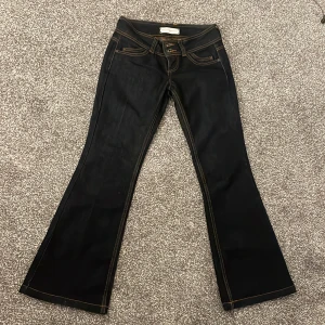 Mörkblåa bootcut jeans - Snygga mörkblåa bootcut jeans med kontrastsömmar och klassisk femficksdesign. De har en låg midja och stängs med dragkedja och knappar. Perfekta för en stilren look.