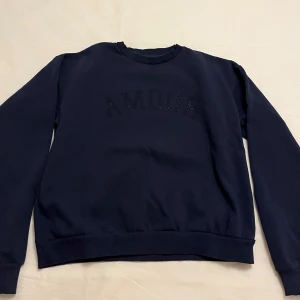 Mörkblå sweatshirt med texten 'AMOUR' - Snygg mörkblå sweatshirt med texten 'AMOUR' i subtila pärlor på bröstet. Tröjan har långa ärmar och en klassisk rund halsringning. Perfekt för en avslappnad stil. Från Gina. 