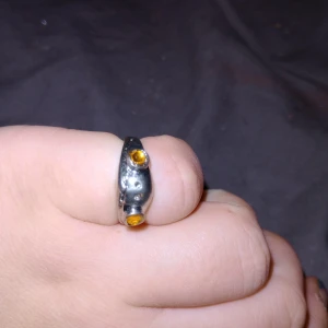 Silverring med gula stenar - Elegant silverring med två gula stenar infattade på framsidan. Ringen har en modern design med en slät yta och en justerbar öppning för perfekt passform. Perfekt för att lägga till en touch av färg och stil till din look.