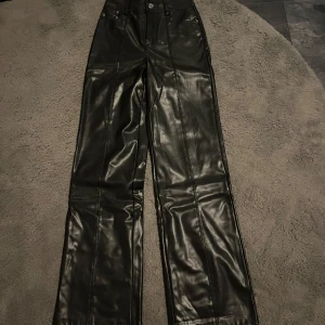 Svarta skinnbyxor - Snygga svarta skinnbyxor med hög midja och lite utsvängda ben nere. Perfekta för en stilren look. Byxorna har en knapp och dragkedja framtill. Lång i längden, aldrig använd 