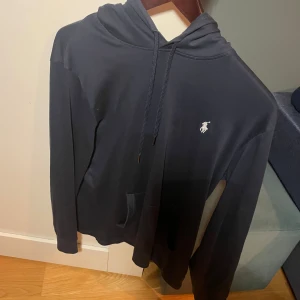 Mörk blå  hoodie från Polo Ralph Lauren - Säljer en stilren mörk blå hoodie från Polo Ralph Lauren med det klassiska logotypen på bröstet. Tröjan har en justerbar huva med snören och en praktisk ficka framtill. Perfekt för en avslappnad look.