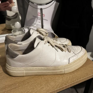 Vita sneakers med grå detalj - Snygga vita sneakers från J.Lindeberg med grå detalj på hälen. Skorna har klassisk snörning och en stilren design. Perfekta för en avslappnad stil. Nypris ligger på 2000kr. Säljer pga lite för stora