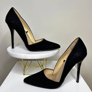 Svarta pumps med spetsig tå - Eleganta svarta pumps med hög klack och spetsig tå. Perfekta för en stilren look. Tillverkade i ett faux mocka material.