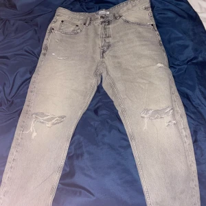 Grå jeans från Zara - Snygga grå jeans från Zara med slitna detaljer på framsidan. De har en klassisk femficksdesign och är tillverkade i denim. Perfekta för en avslappnad stil.