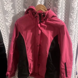 Rosa och lila vinterjackor med huva - Två snygga vindjackor i rosa och lila med svarta detaljer. Båda har huva och dragkedja framtill samt praktiska fickor med dragkedjor. Perfekta för blåsiga dagar och utomhusaktiviteter. 