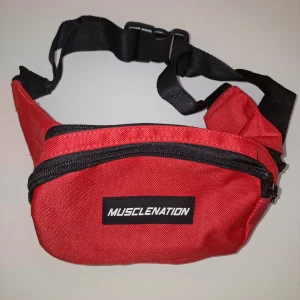 Röd midjeväska från Musclenation - Snygg och praktisk röd midjeväska från Musclenation. Väskan har ett justerbart svart bälte och dragkedja för säker förvaring. Perfekt för att hålla dina saker nära till hands när du är på språng. Garderobsrensning så kika gärna på övriga auktioner.