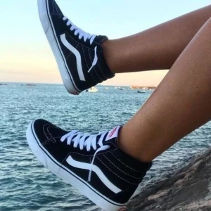 Vans skor - Klassiska svarta sneakers från Vans med vit sula och vit sidostrimma. Skorna har snörning och en högre skaftdesign som ger en cool och tidlös look. Perfekta för en avslappnad stil.