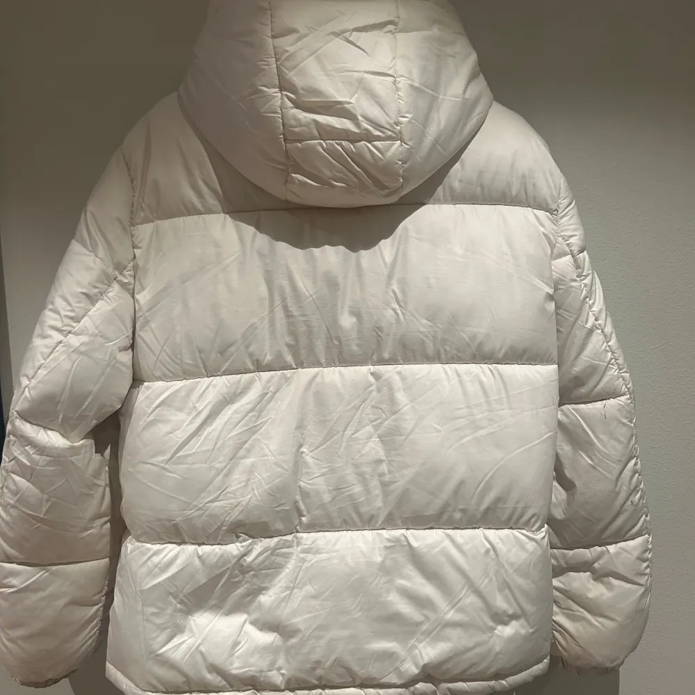 Säljer en snygg vit pufferjacka från H&M. Jackan har en dragkedja framtill och en mysig huva med snörning. Perfekt för kyliga dagar med sin vadderade design och långa ärmar.. Takit.