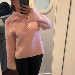 Rosa stickad polotröja - Mysig rosa stickad polotröja med ribbad struktur. Perfekt för kyliga dagar med sin höga krage och armar med slits 