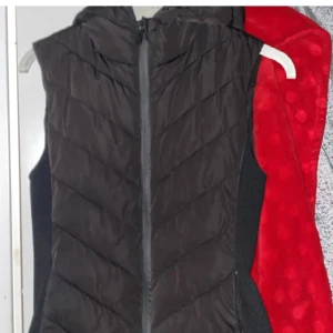 Svart dunväst med dragkedja - Snygg svart dunväst med dragkedja framtill. Perfekt för lager-på-lager under kyliga dagar. Västen har en stilren design och är lätt att matcha med olika outfits.