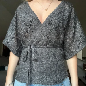 Grå omlottopp med knytband - Snygg grå omlottopp/kimono med knytband i midjan. Toppen har korta ärmar och genombrutet,  glittrigt mönster💗 Passar xs-m💗