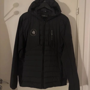 Svart dunjacka från Sail Racing - Säljer en svart dunjacka från Sail Racing med huva och dragkedja. Jackan är tillverkad med Allied Feather + Down och har 800 fill power. Den är vattentät, andas och har stretch i alla riktningar. Kom privat för fler bilder 🙌.