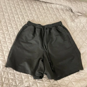Svarta shorts med dragsko - Säljer ett par svarta shorts med elastisk midja och dragsko för justerbar passform. Perfekta för en avslappnad stil. De är enkla och stilrena, vilket gör dem lätta att matcha med olika outfits.