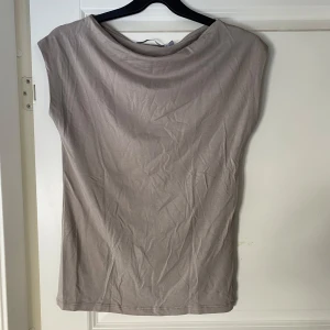 Beige ärmlös topp - Säljer en  beige ärmlös topp i mjukt material. Perfekt till både fest och vardags.  Toppen har en enkel design med rund hals och är i superfint skick. 