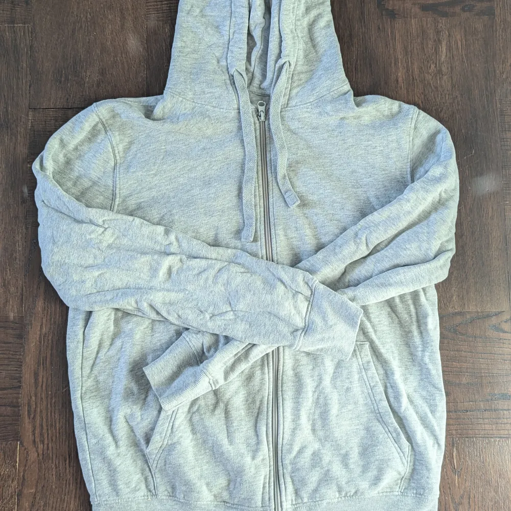 Säljer en grå hoodie i mjukt material med dragkedja framtill. Perfekt för en avslappnad stil och passar till alla årstider. Den har långa ärmar och en praktisk huva. Perfekt för mysiga dagar eller som ett extra lager när det är kyligt. . Hoodies.