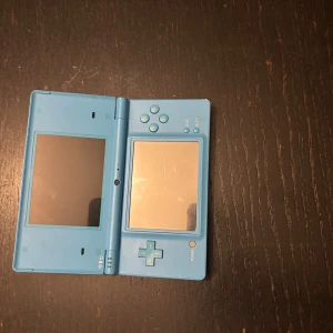 Blå Nintendo DS - Säljer en blå Nintendo DS i fint skick. Den har dubbla skärmar och klassiska knappar för en nostalgisk spelupplevelse. Perfekt för dig som älskar retro gaming eller vill återuppleva gamla favoriter. Konsolen är portabel och lätt att ta med sig överallt. Passa på att köpa denna ikoniska spelkonsol! Laddare kommer tyvärr inte med