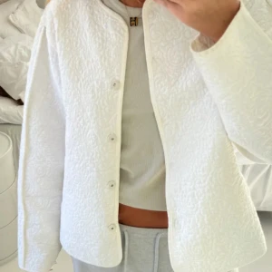Vit quiltad jacka - Säljer en superfin vit quiltad jacka med knappar framtill. Den är perfekt för vår och höst, och ger en stilren look. Jackan har långa ärmar och en normal passform. Perfekt för att lyfta vilken outfit som helst!
