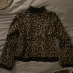 Leopardmönstrad stickad tröja - Säljer en supercool leopardmönstrad stickad tröja med svarta ribbade detaljer vid hals, ärmslut och nederkant. Perfekt för att liva upp din höst- och vintergarderob. Tröjan är både varm och trendig, idealisk för kyliga dagar. 🐆✨