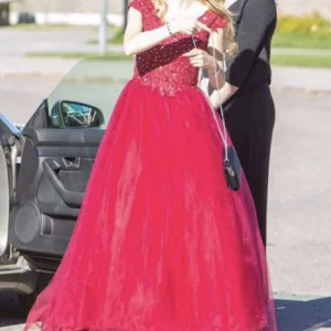 Vinröd balklänning - Fantastisk vinröd balklänning med pärlor på överdelen. Klänningen har en vacker v-ringning och är ärmlös, perfekt för festliga tillfällen. Den långa kjolen ger en elegant look och passar perfekt för bal eller andra festliga tillfällen. Den är i storlek 34-36.