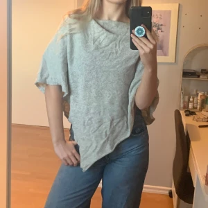 Grå poncho i mjukt material - Säljer en supermysig grå poncho i mjukt material. Perfekt för kyliga dagar och ger en avslappnad look. Den har en lös passform och är lätt att slänga över vilken outfit som helst. Perfekt för höst och vår!