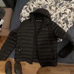 Svart dunjacka från Wyte - Säljer en svart dunjacka från Wyte i mycket bra skick. Jackan är perfekt för höst och vinter med sin varma och quiltade design. Den har en praktisk huva och dragkedja framtill. Passar både till vardags och lite mer uppklädda tillfällen. Superbekväm och stilren!