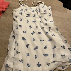 Vit klänning med fjärilsmönster från H&M Divided - Säljer en superfin vit klänning från H&M Divided med blå fjärilar. Den har smala axelband och en söt knytning framtill. Perfekt för sommardagar eller en avslappnad vårdag. Klänningen är i mycket bra skick och redo för nya äventyr! 🦋