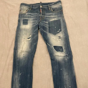 Blåa jeans från Dsquared2 (storlek 48) - Säljer ett par coola blå jeans från Dsquared2 i storlek 48. Nypris ca 6000kr säljes för 2500kr, nyskick, enbart använd vid 2-3 tillfällen! De har en häftig look och färgstänk för en edgy stil. Perfekta för en avslappnad och trendig outfit. Passar bra till både vardag och fest!