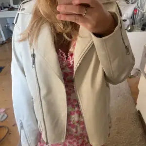 Säljer en snygg beige skinnjacka i mycket bra skick. Den har en cool dragkedja framtill och på ärmarna, vilket ger den en edgy look. Perfekt för vår och höst! Jackan har en normal passform och är långärmad. Passar perfekt till både vardag och fest.