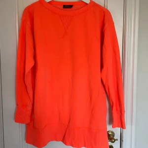 Tröja från Polo Ralph Lauren - Säljer en snygg och färgglad orange tröja från Polo Ralph Lauren i storlek XS (stor i storleken). Färgen stämmer inte överens med bilden då den i verkligheten är i mjukare nyans. Tröjan har långa ärmar och en ribbad kant vid ärmslut och nederkant. Perfekt för att liva upp garderoben! 🧡 