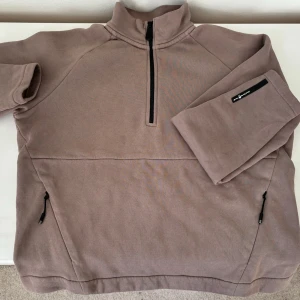 Beige tröja från Sail Racing - Säljer en snygg beige tröja från Sail Racing i mycket bra skick. Den har flera fina detaljer med en halfzip framtill och  fickor med dragkedjor på sidorna samt dekorativa märken på ärmen och nacken. En rak, kortare modell utan muddar. 