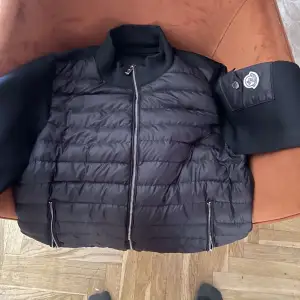 Säljer en snygg svart pufferjacka från Moncler. Jackan har en quiltad design med dragkedja framtill och långa ärmar. Perfekt för höst och vinter, håller dig varm och stilren. Den har en cool Moncler-logga på ärmen. Skriv till mig om priset eller bilder pris kan diskuteras. Den är ny knappt använd