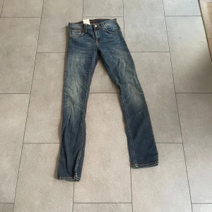 Nudie Jeans ”Tube Tom” - Säljer ett par snygga blå jeansbyxor i bra skick. De har en klassisk femficksdesign och en bekväm passform. Perfekta för vardagsbruk och kan enkelt matchas med olika outfits. Passar både till avslappnade och mer uppklädda tillfällen. W:27 L:32. Färg: ”Blue Nights”