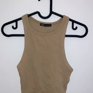 Beige ribbad linnetopp från Zara - Säljer en snygg beige ribbad linnetopp från Zara. Perfekt för sommardagar eller som ett basplagg i garderoben. Toppen är ärmlös och har en tight passform som framhäver figuren. Superbekväm och lätt att matcha med olika outfits!
