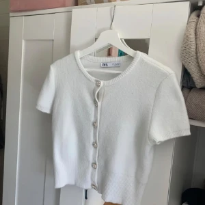 Vit kofta från Zara med glittriga knappar - Säljer en superfin vit kofta från Zara i storlek M, men liten i storleken så passar mig som har XS. Den har korta ärmar och är dekorerad med glittriga knappar som ger en lyxig touch. Perfekt för både vardag och fest! 🕊✨