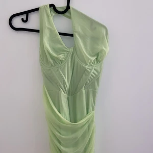 Ljusgrön klänning - Säljer en superfin ljusgrön klänning i syntetmaterial. Den har en tight passform och är ärmlös med en snygg drapering framtill. Perfekt för sommarens fester eller en utekväll. Klänningen är i mycket bra skick och redo att bäras av någon som vill sticka ut!