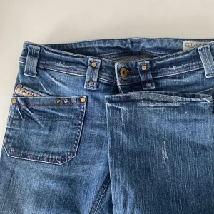 Blå jeans från Diesel - Säljer ett par snygga blå jeans från Diesel i modellen Larkee. De har en klassisk femficksdesign med coola stjärndetaljer på bakfickan. Jeansen är i bra skick och har en bekväm passform. Perfekta för både vardag och fest!