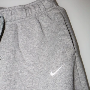 Grå mjukisbyxor från Nike - Säljer ett par grå mjukisbyxor från Nike i mycket bra skick. De har en bekväm passform med resår och snörning i midjan. Perfekta för en avslappnad dag hemma eller lätt träning. Nike-loggan är broderad på sidan. Supermjuka och sköna!