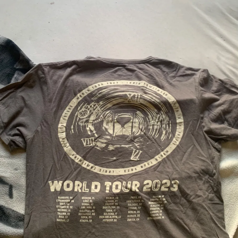 Säljer  t-shirt från Louis Tomlinson med texten 'Faith in the Future' på framsidan och 'World Tour 2023' med turnédatum på baksidan. T-shirten är i bomull och har en liten reva i armhålan inte alls synlig . Perfekt för fans av Louis Tomlinson!. T-shirts.