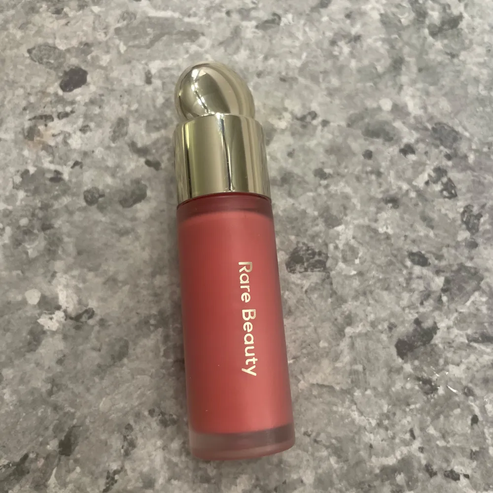 Säljer en superfin flytande rouge från Rare Beauty i nyansen Happy. Den har en härlig rosa färg och kommer i en elegant flaska med guldfärgat lock. Perfekt för att ge kinderna en fräsch och naturlig look. Innehåller 7,5 ml och ger en naturlig och jämn finish. Köptes för 389 kr. Skönhet.